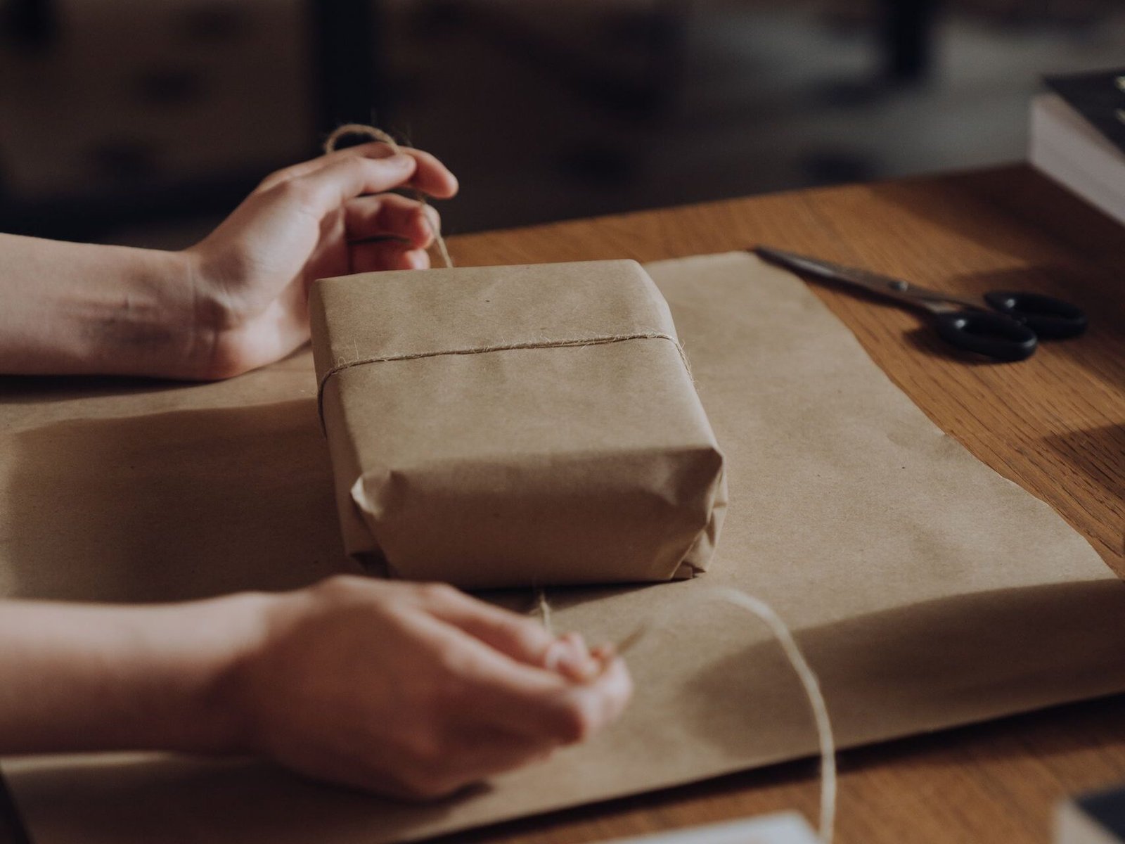 Hands skillfully wrapping a book with brown craft paper in a bookstore setting.